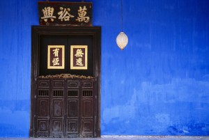 Malaysia, Penang, Georgetown, Cheong Fatt Tze Mansion. Restored Chinese merchants house. Wooden doorway with gold Chinese letters set into blue painted wall with lantern hanging at side.